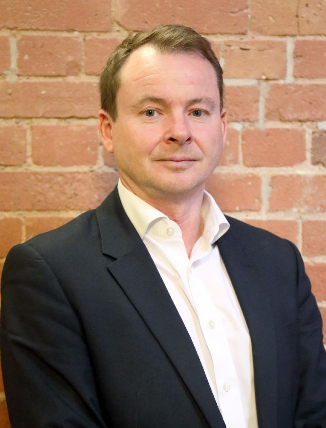 In front of a brick wall Rob McGuinn stands in a black suit representing Team Leicester. He works at MDA property consultancy 
