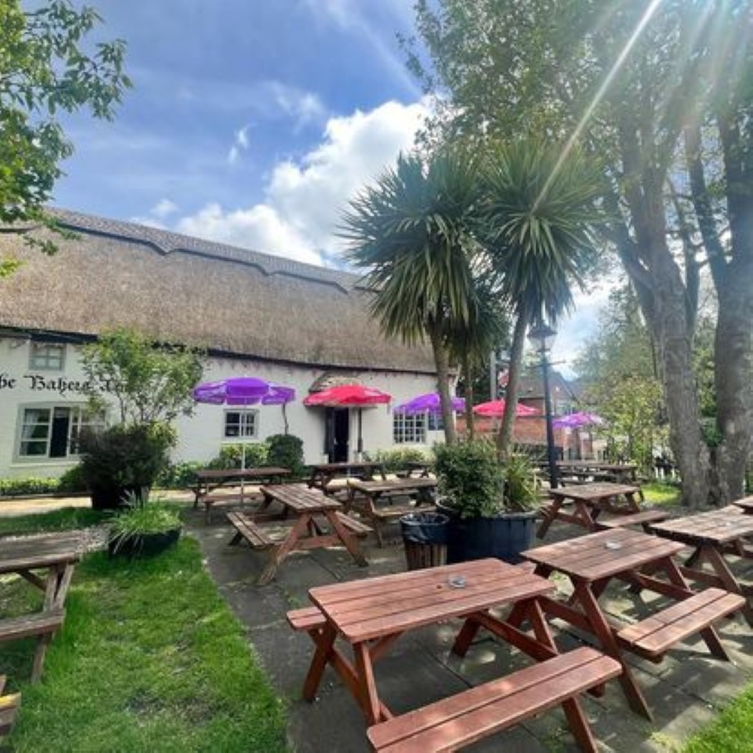 garden with beer benches in front of a thatched pub