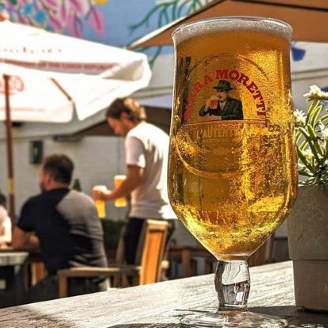 a cold pint of beer in front of two people in a pub garden